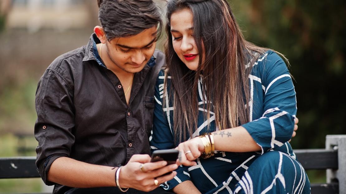 زن و مردی به صفحه گوشی موبایل نگاه می کنند.